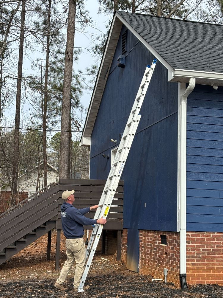 wildlife-bat-possum-removal-columbia-sc Jeffcoat tech setting up an extension ladder against a blue house with brick foundation and white trim.