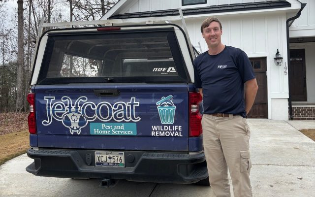 professional-flea-treatment-columbia-south-carolina Jeffcoat Pest and Home Services tech standing beside branded dark blue pickup truck with canopy in residential driveway; house with white siding and brick foundation in background.