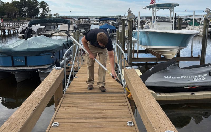 best-monthly-pest-control-business-commercial-columbia-sc Jeffcoat tech n dock using long tool near moored boats; calm water, American flag, partly cloudy sky.